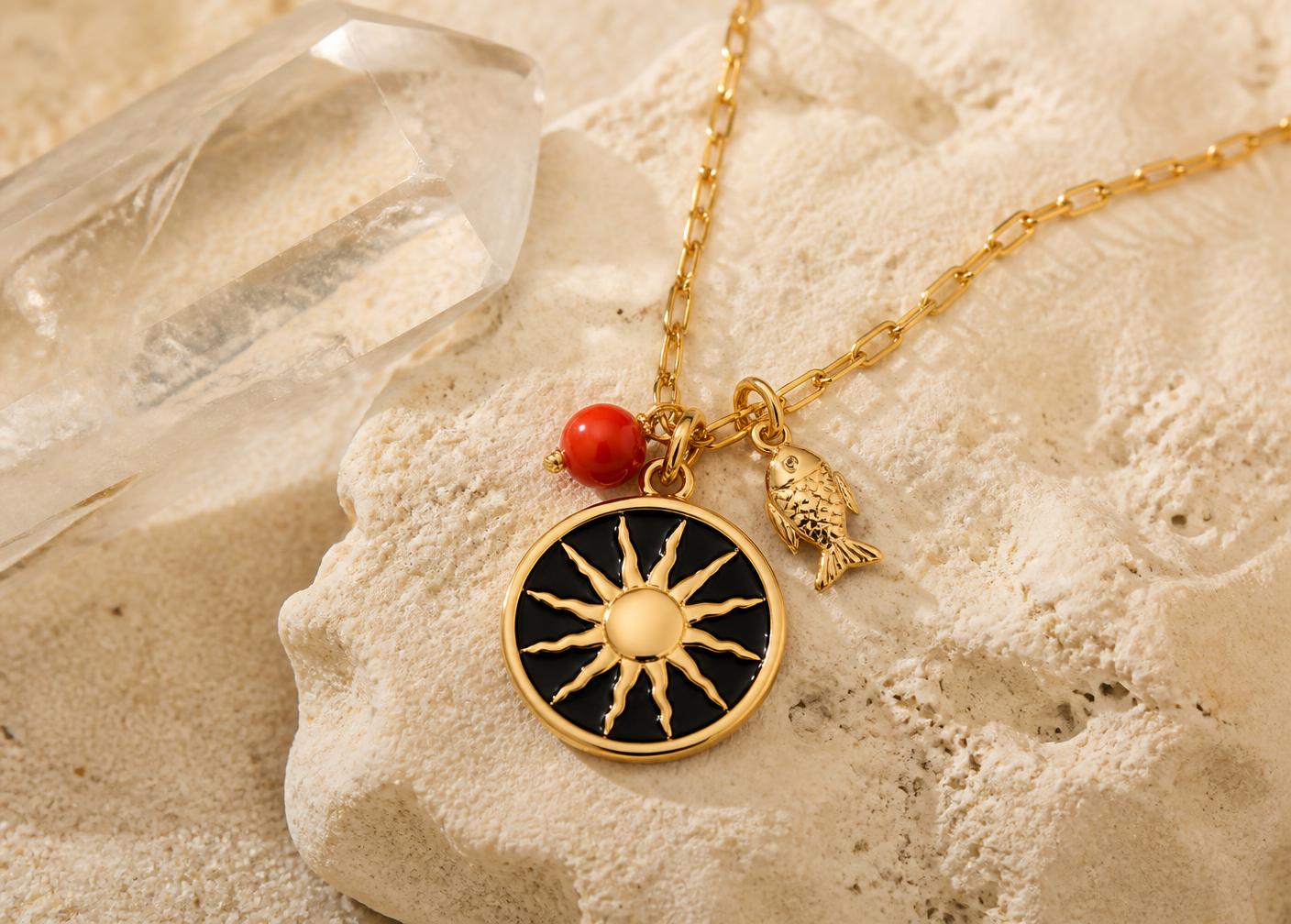 Gold sun medallion necklace with coral bead and fish charm on coral rock